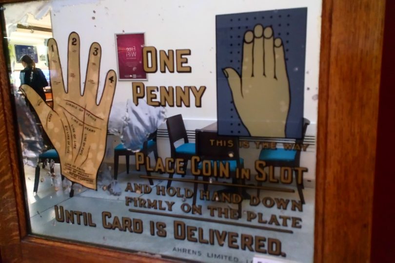 Part of an early twentieth century pier or arcade machine. The sign promises to read the user's palm for one penny, and gives instructions.